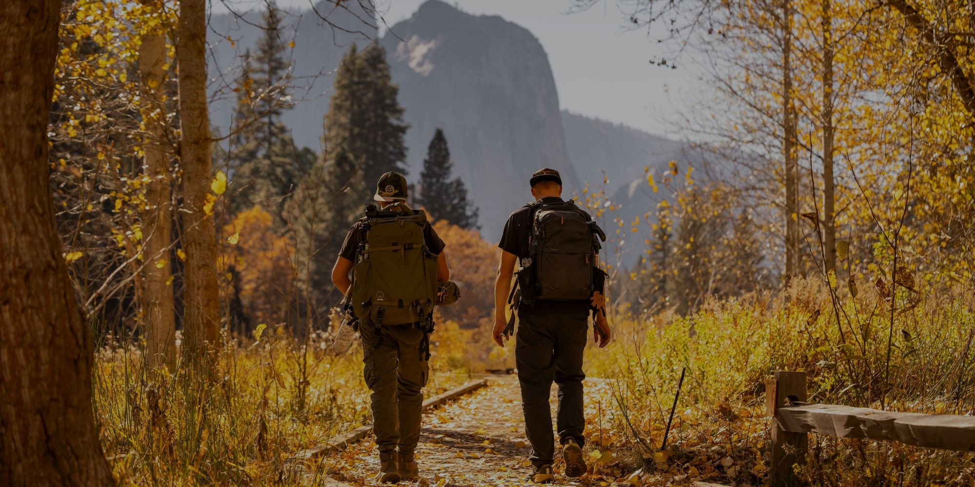 Two hikers walking along a trail in a mountainous forest during autumn.